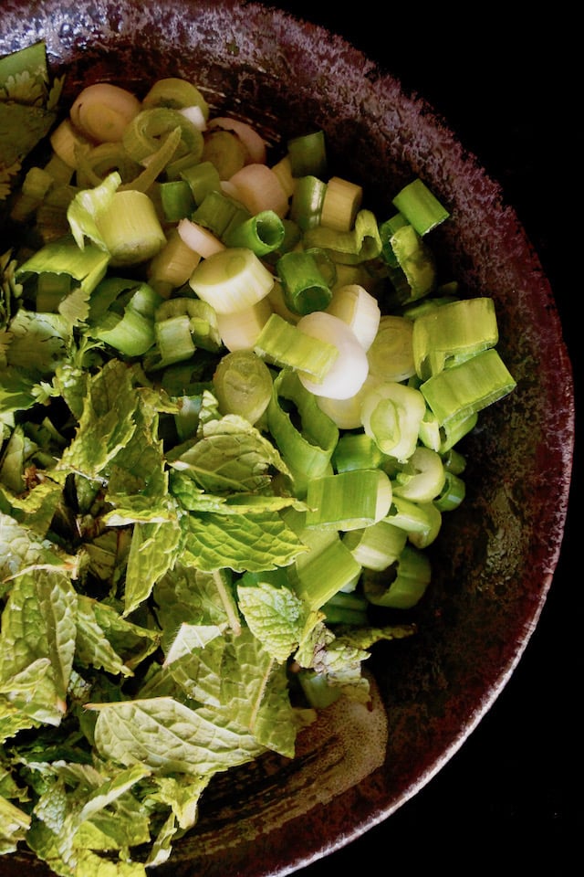 Fresh mint, cilantro and scallions in a black bowl.