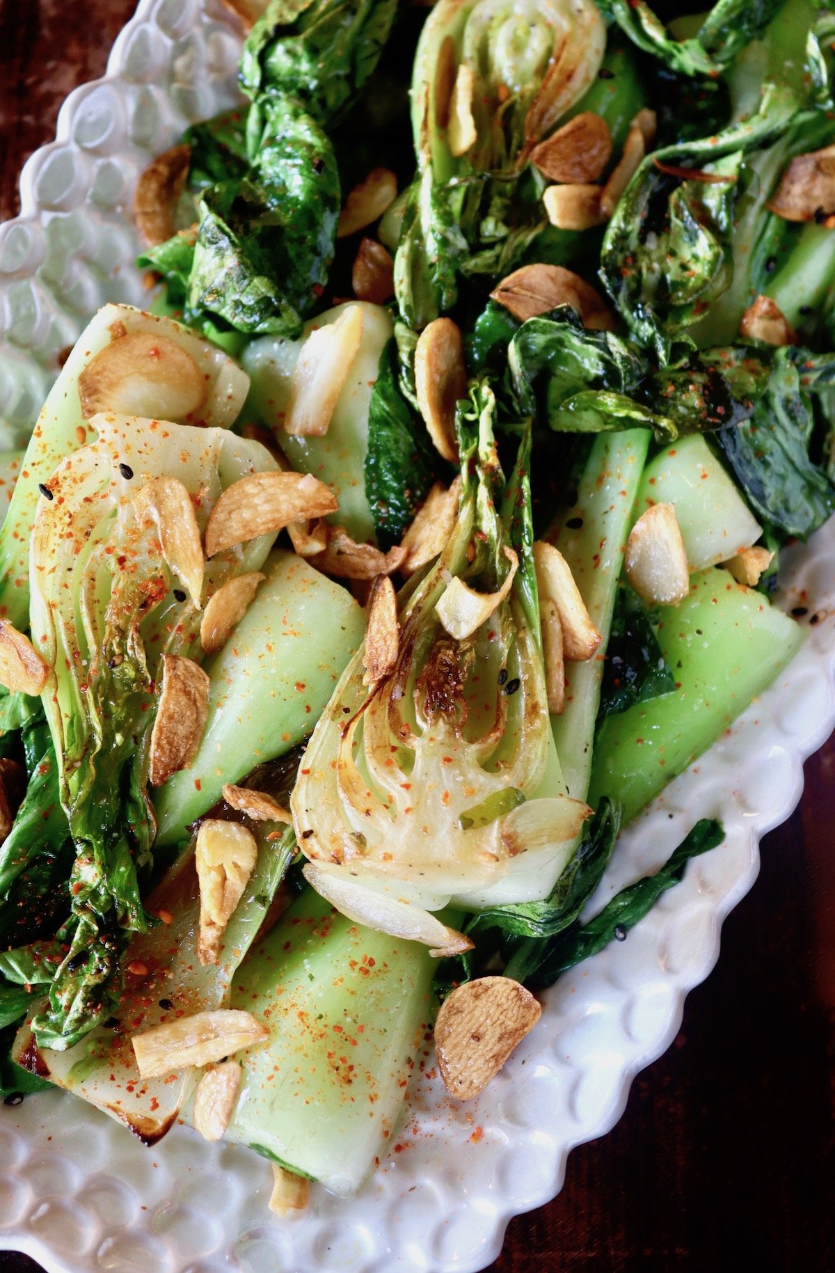 Top view of sauteed bok choy with bits of garlic on white platter.
