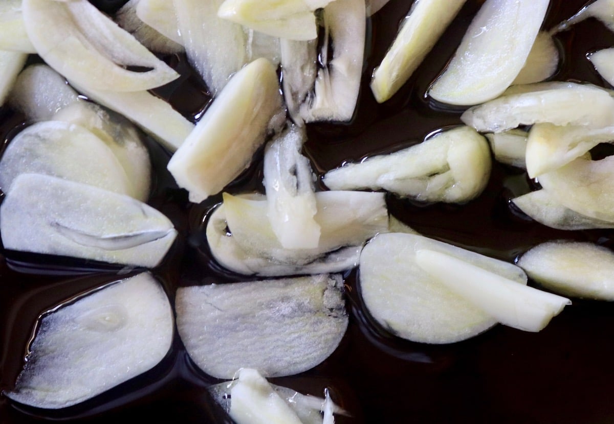 Raw, thin slices of garlic in saute pan.