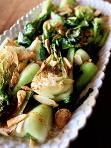 Sautéed bok choy with bits of crispy garlic on a long and narrow white platter.