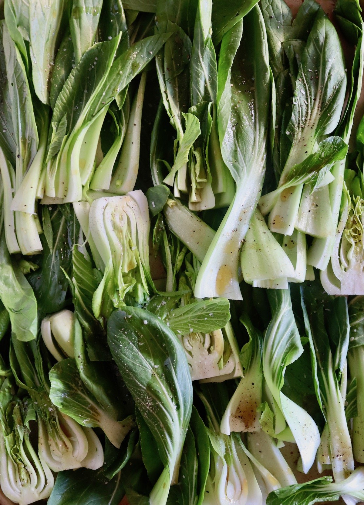 Sheet pan full with baby bok choy sliced in half with oil drizzled over it.