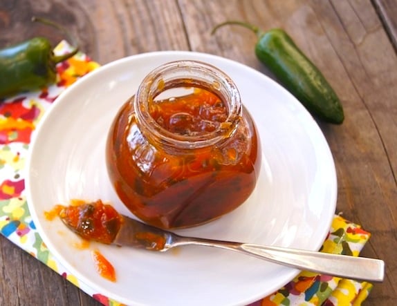 Grapefruit Jalapeno Marmalade in a small jar on a white plate, on a wooden table with a brightly colored cloth.