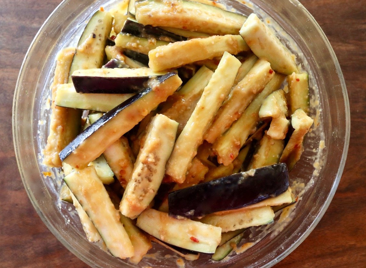 Raw eggplant sticks in a large glass bowl coated in miso marinade.