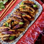 Blue and white rectangle-shaped plate with miso eggplant and a few fresh mint leaves, on a red silk cloth with chopsticks.
