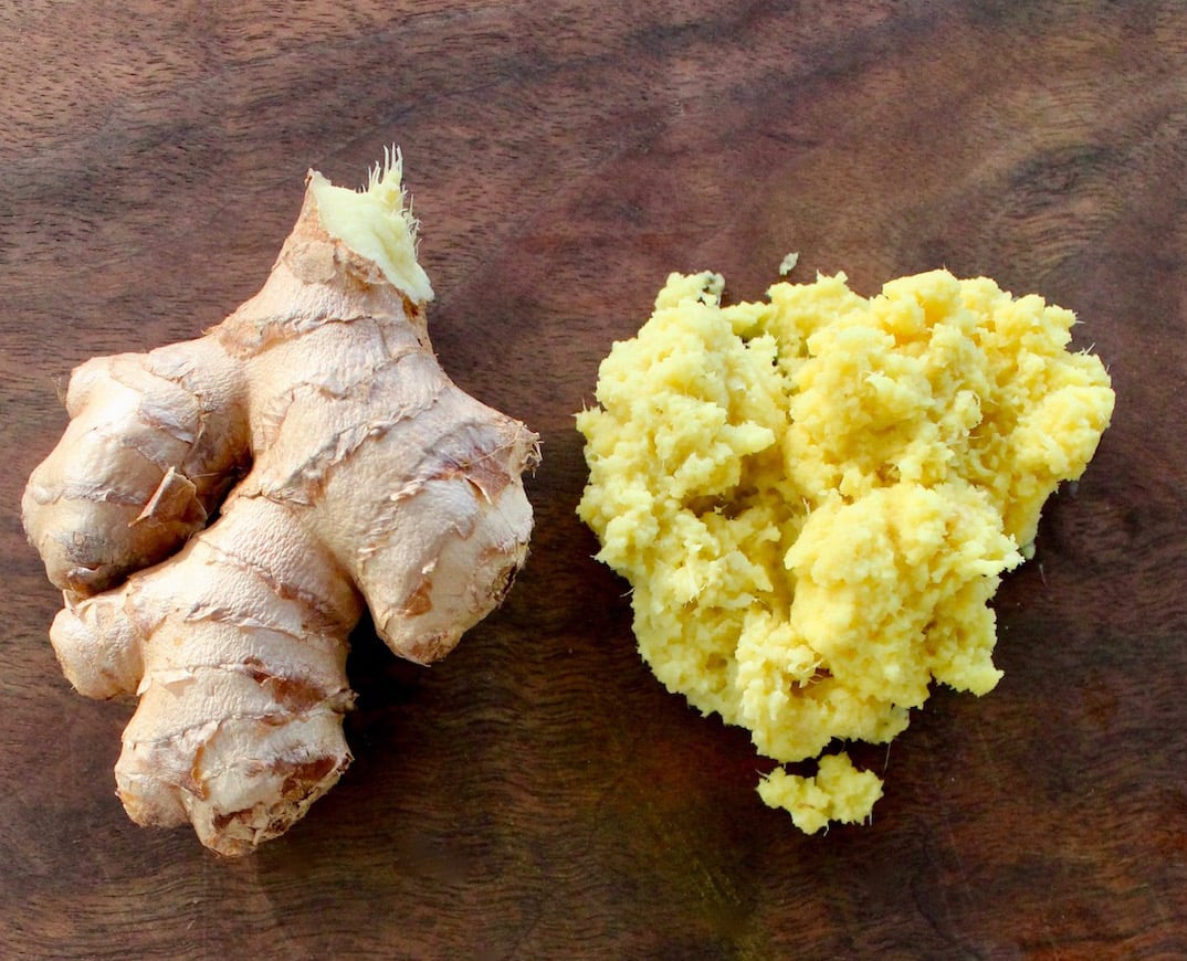 Fresh ginger root and grated giner on a dark wood cutting board.