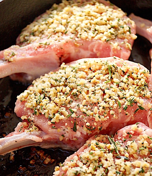 raw pork chops on sheet pan with garlic rosemary mix on top