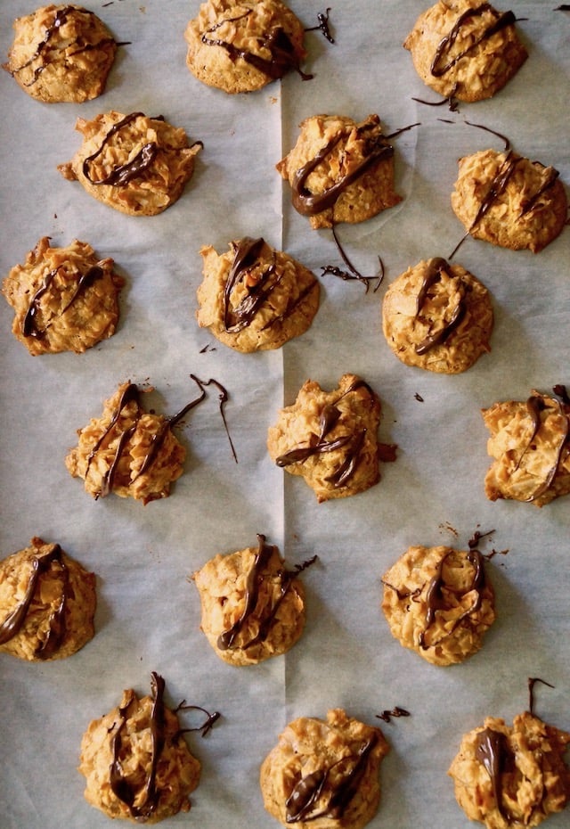 About a dozen Salted Dulce De Leche Coconut Macaroons on prachment, drizzled with chocolate.