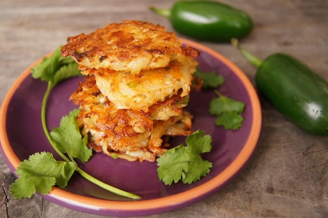 3 crispy potato pancakes on a purple plate with cilantro leaves.