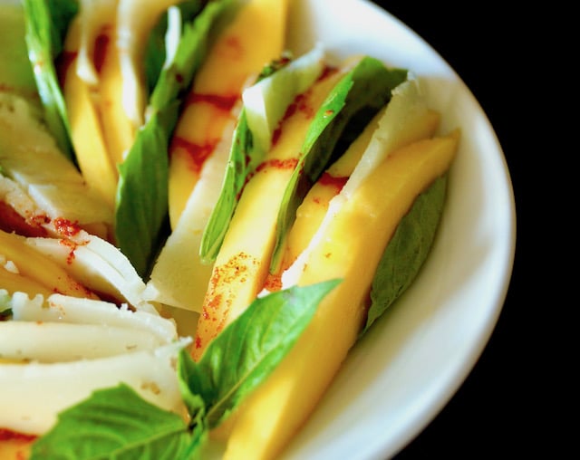 Mango Manchego Basil Salad arranged on a white plate with a reddish dressing drizzled on top.