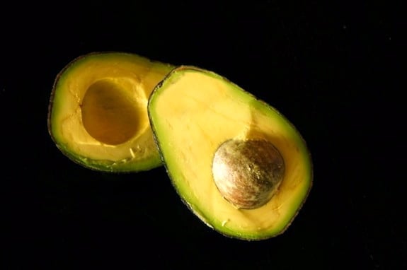 One avocado cut in half with pit
