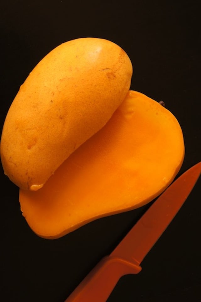 Mango sliced in half with orange knife