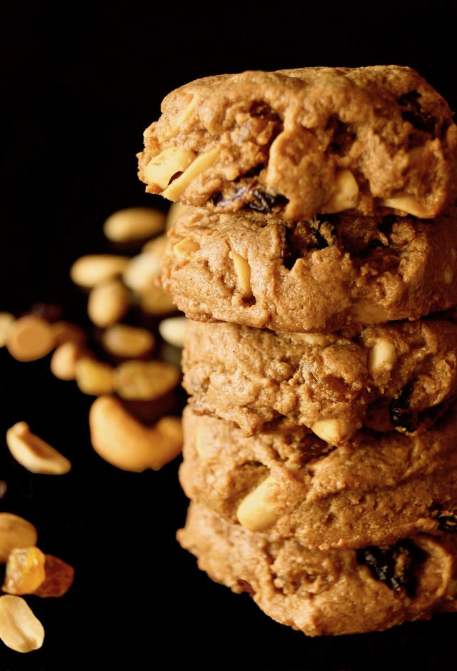 Tall stack of Trail MIx Peanut Butter Cookies with black background with a few nuts.