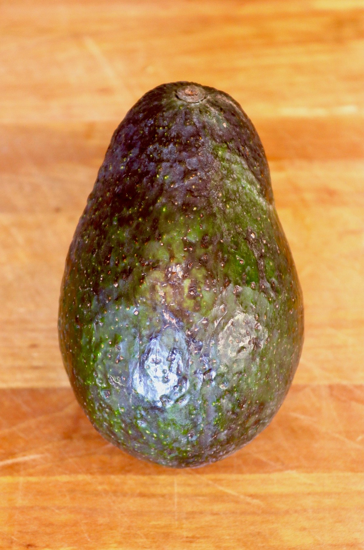 One whole avocado that's a perfect pear shape, on wood cutting board.