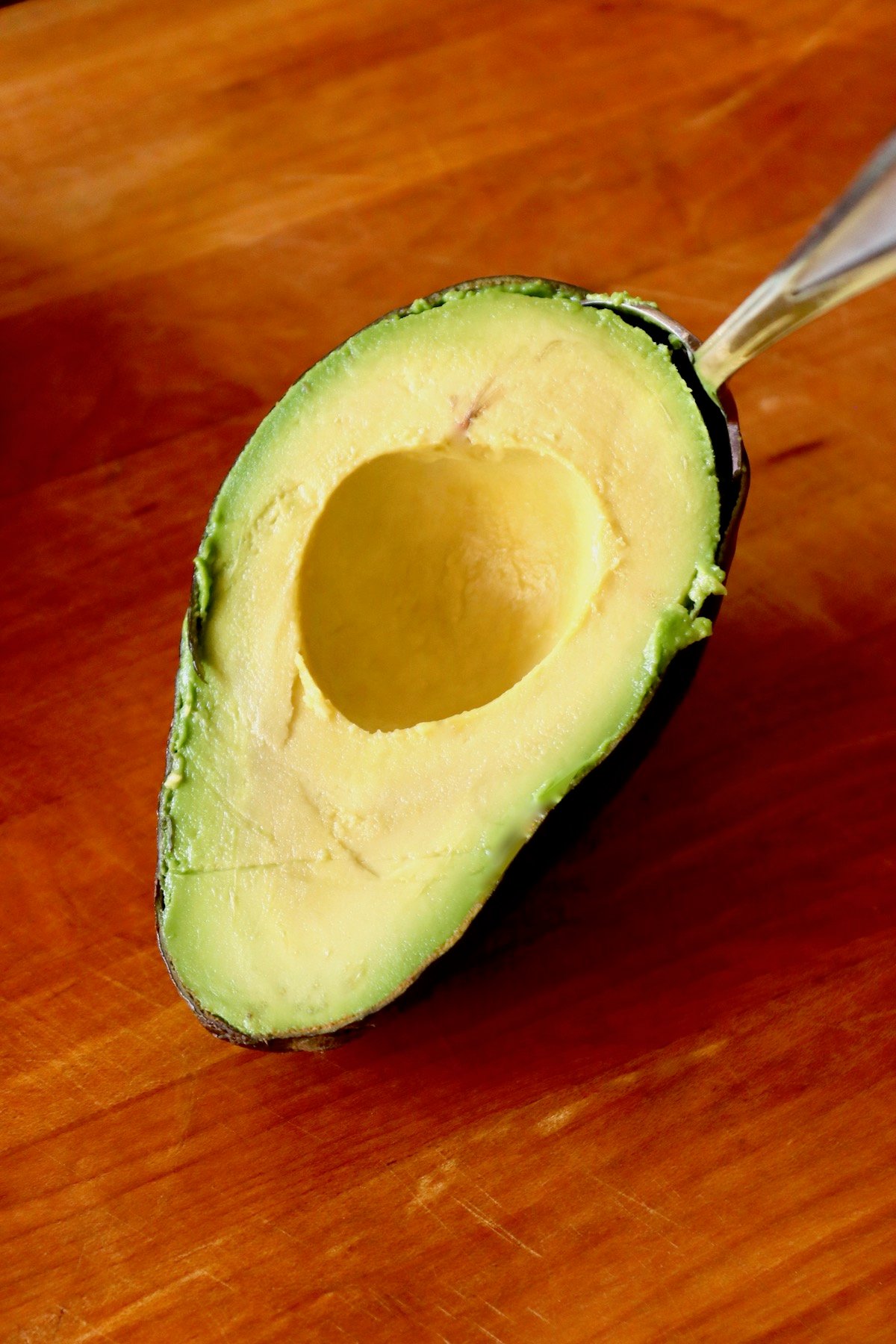 Avocado half with a spoon lifting out the flesh.