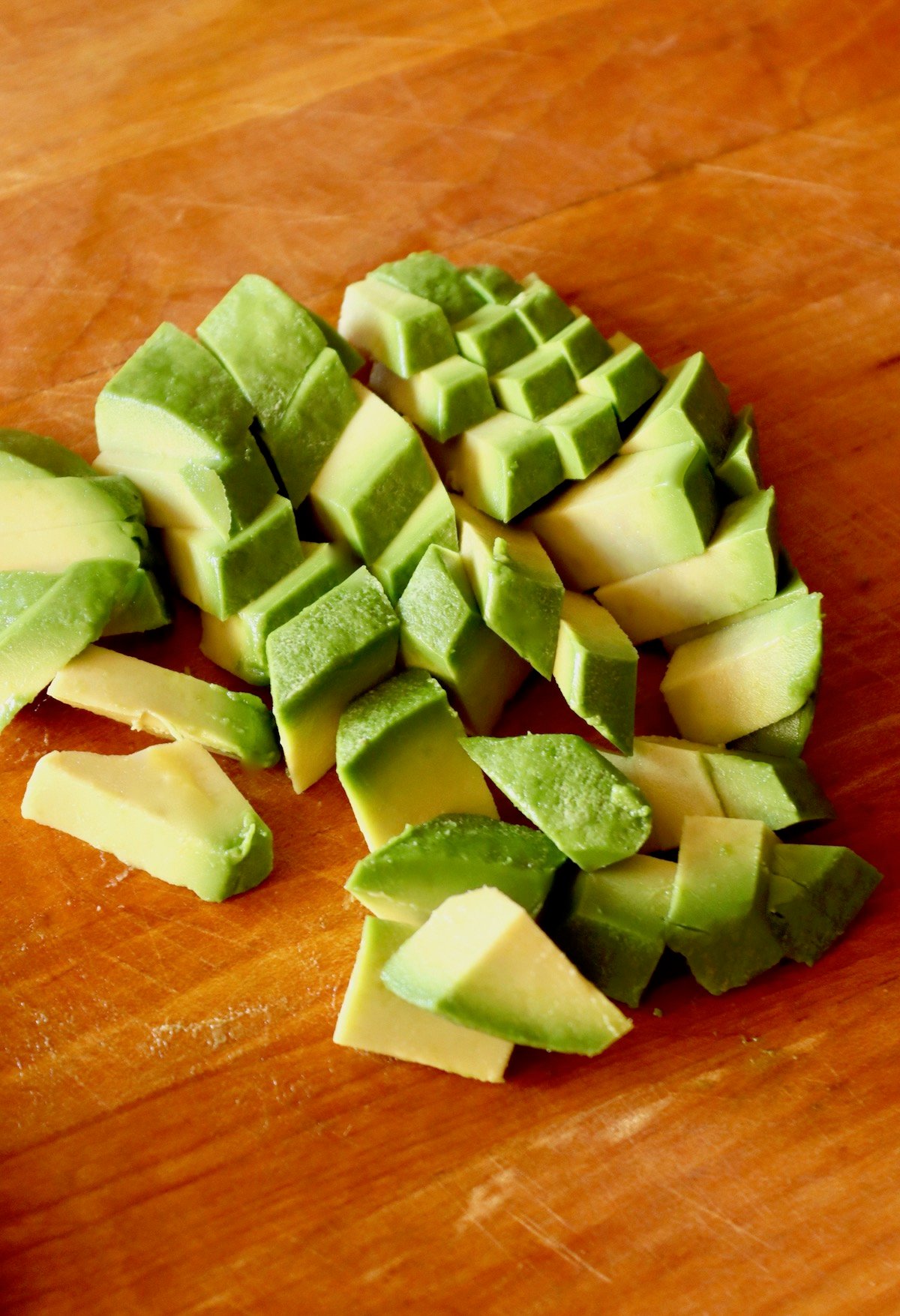 Peeled and diced avocado on a wooden cutting board.