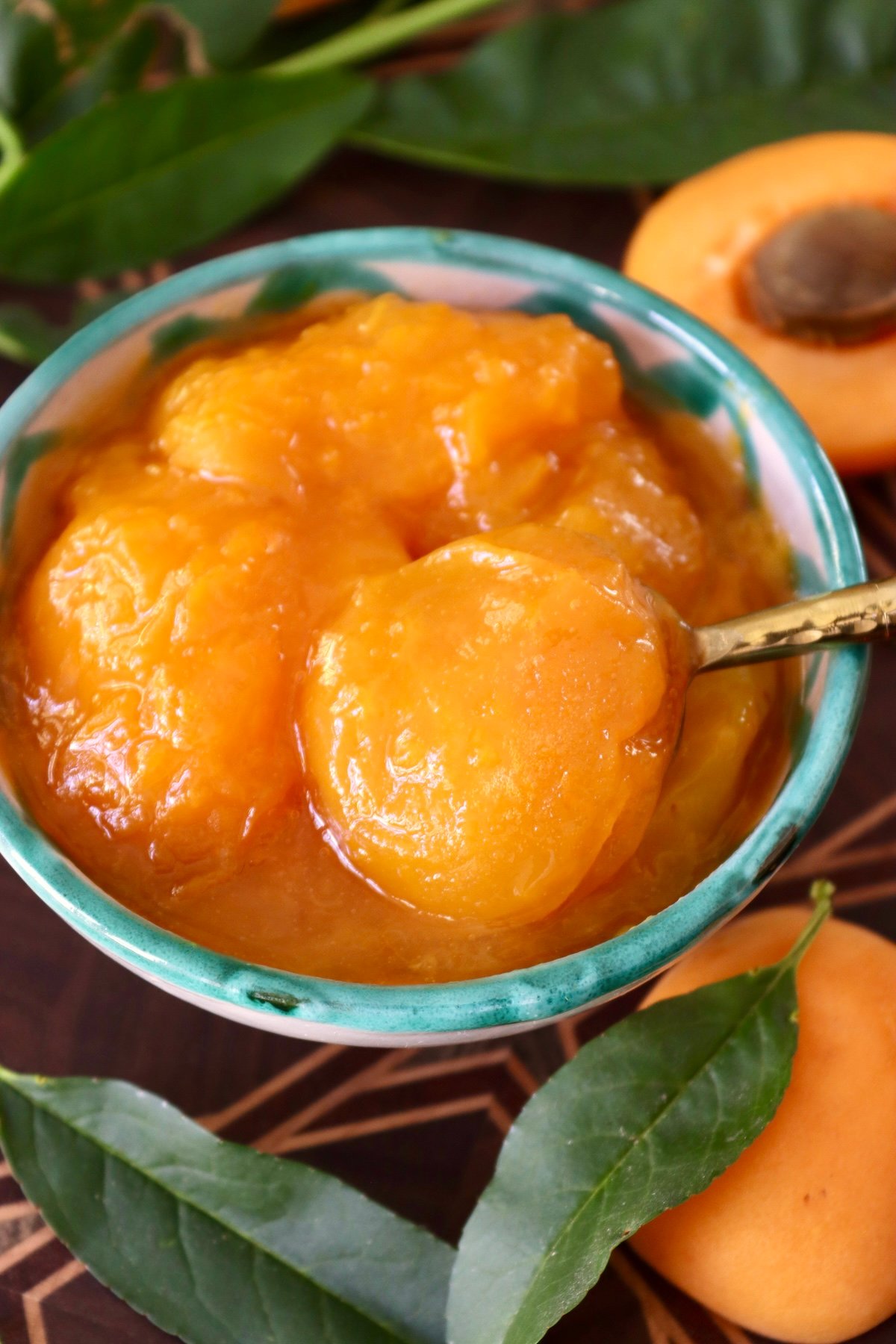 Apricot-Preserves-Recipe Small turquoise-rimmed ceramic bowl fill with chunky apricot preserves and a small golden spoon.