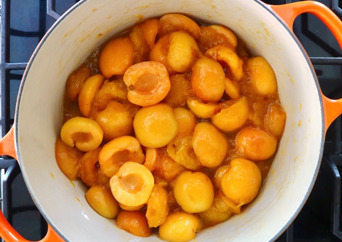 Dutch oven full with apricots halves and apricots that are cooked.