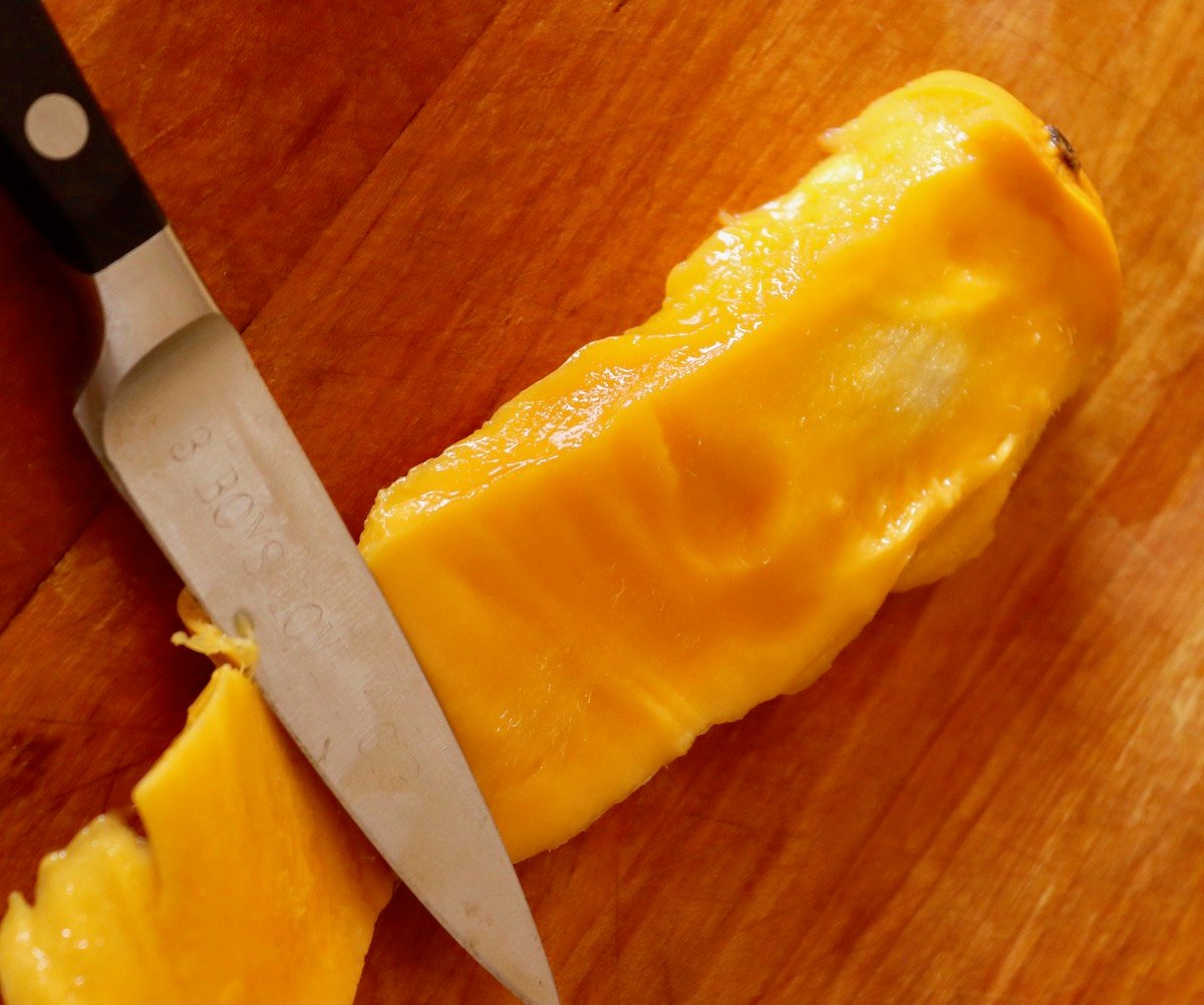 Flesh being cut off from around a mango pit.