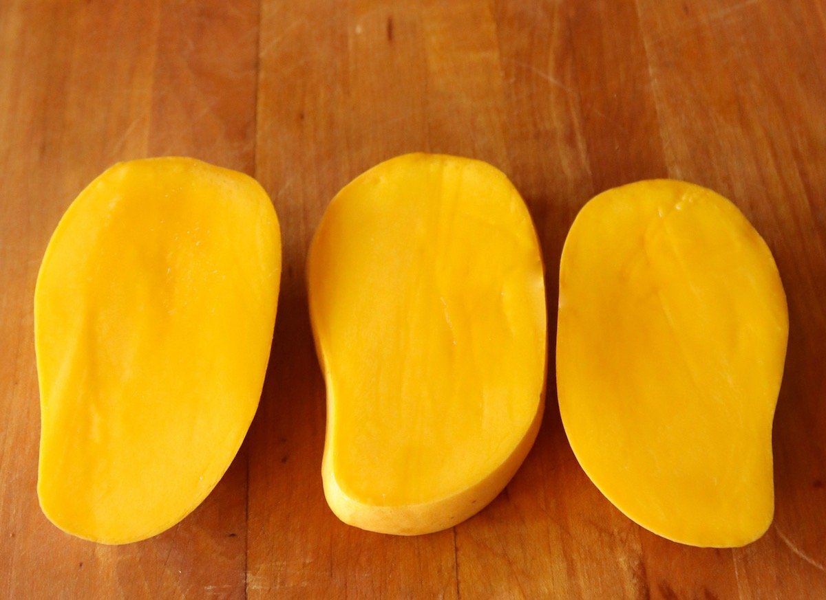 Honey mango sliced into three equal pieces on a cutting board.