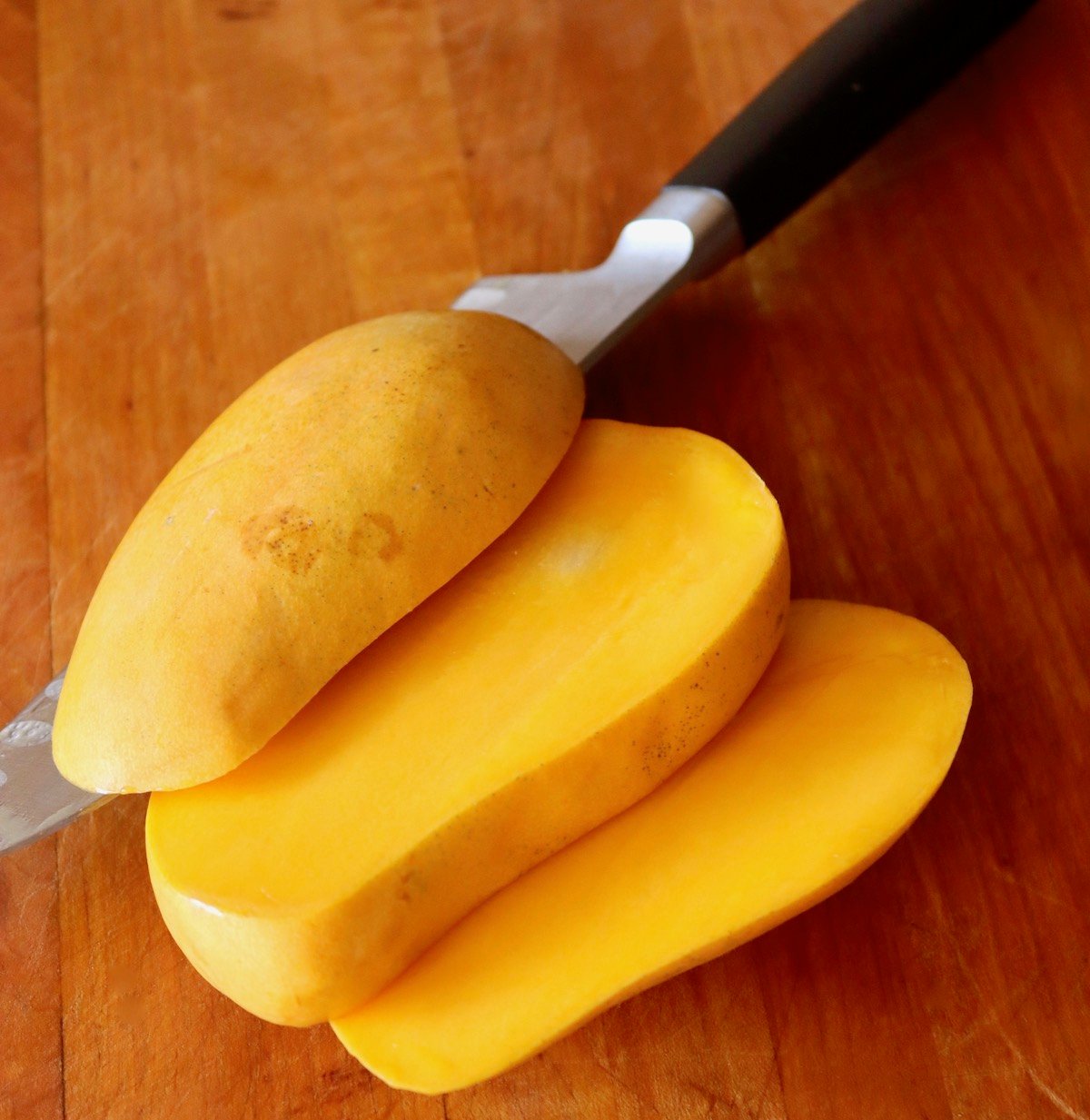 Honey mango sliced into three equal pieces on a cutting board.