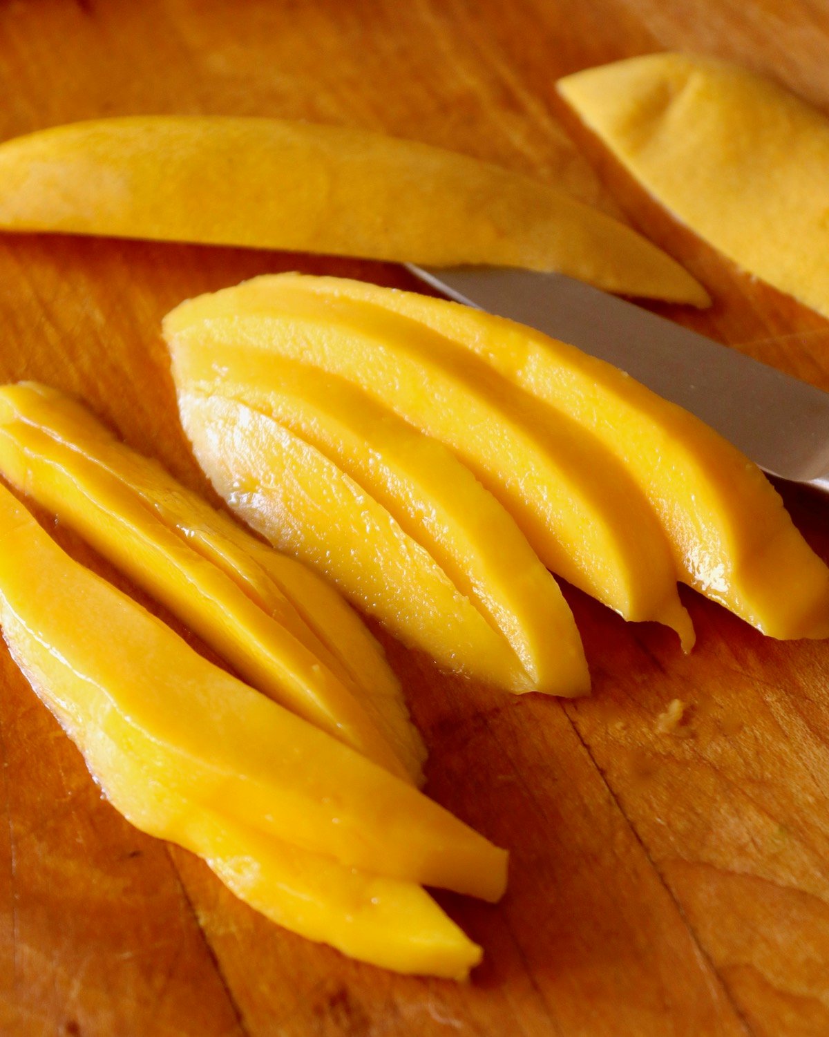 Many long slices of mango on a cutting board.