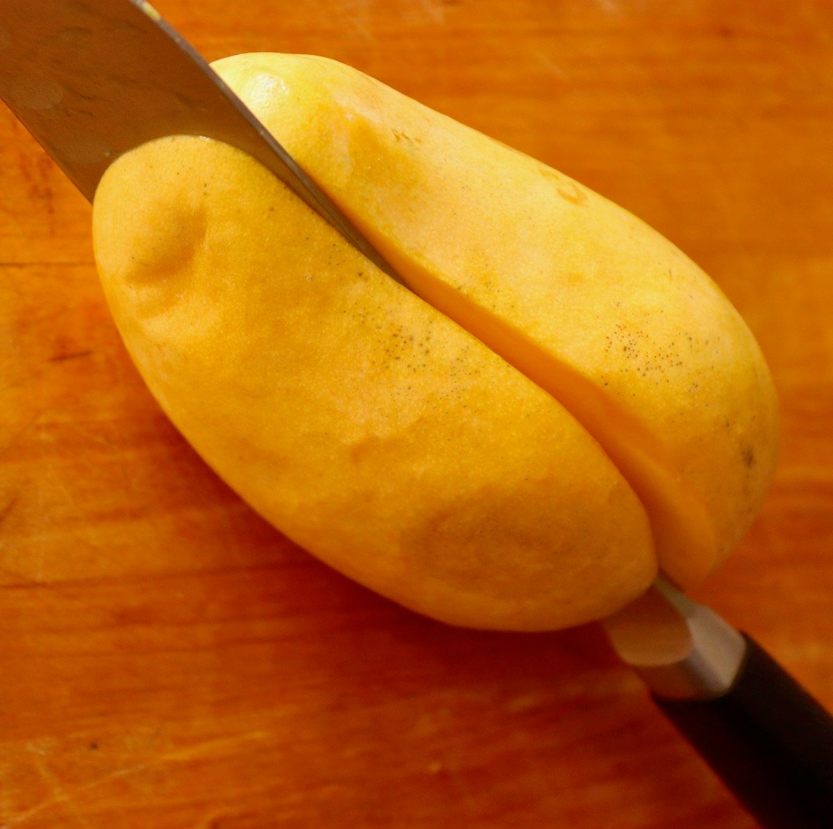 Honey Mango on cutting board with Chef's knife slicing it.