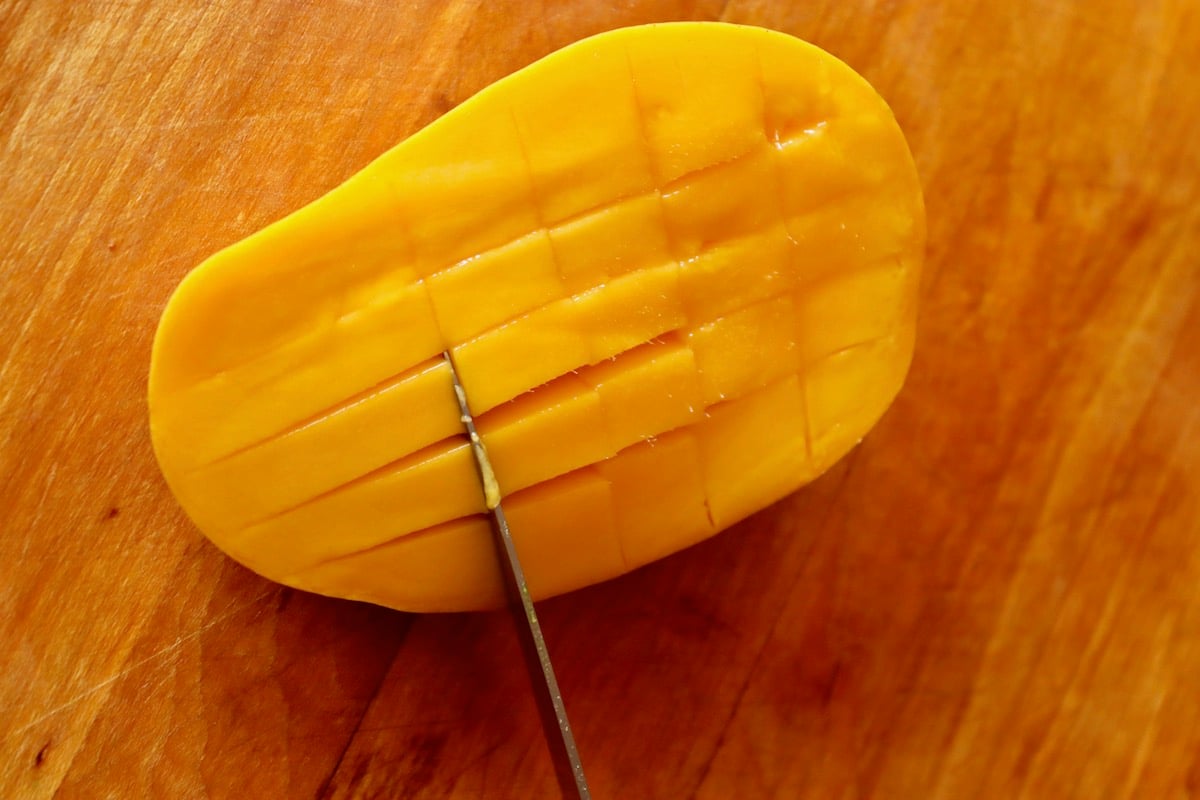 Mango half with skin on being diced.