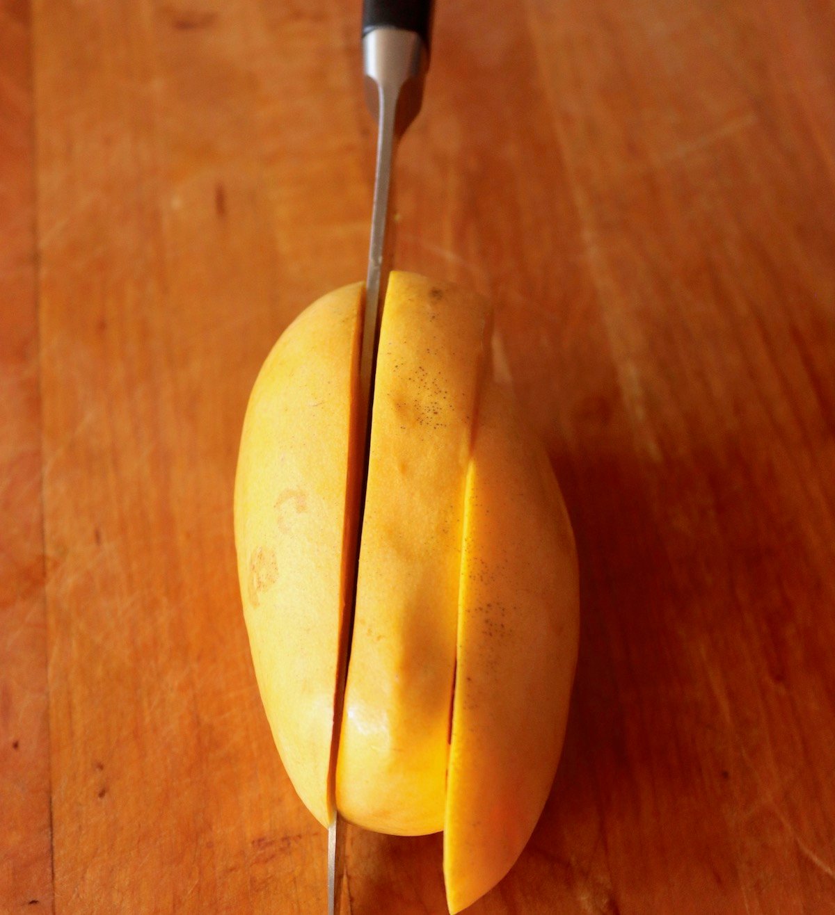 Honey Mango on cutting board in three parts, with Chef's knife slicing it.