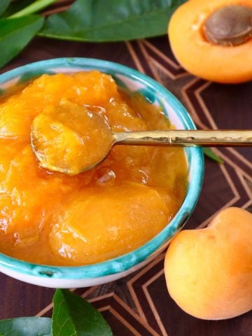 Small turquoise-rimmed ceramic bowl fill with chunky apricot preserves and a small golden spoon.