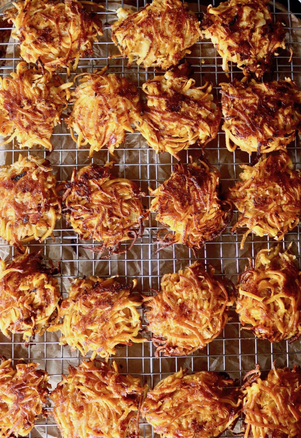 20 crispy, browned sweet potato pancakes on wire baking rack.