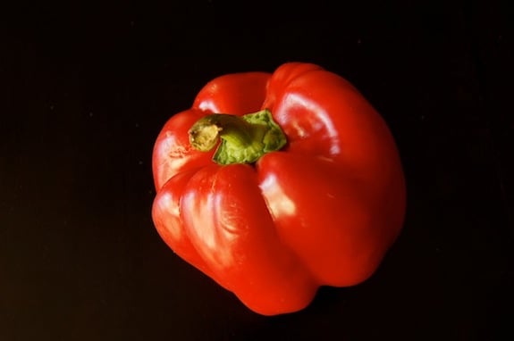 One raw red bell pepper on black background