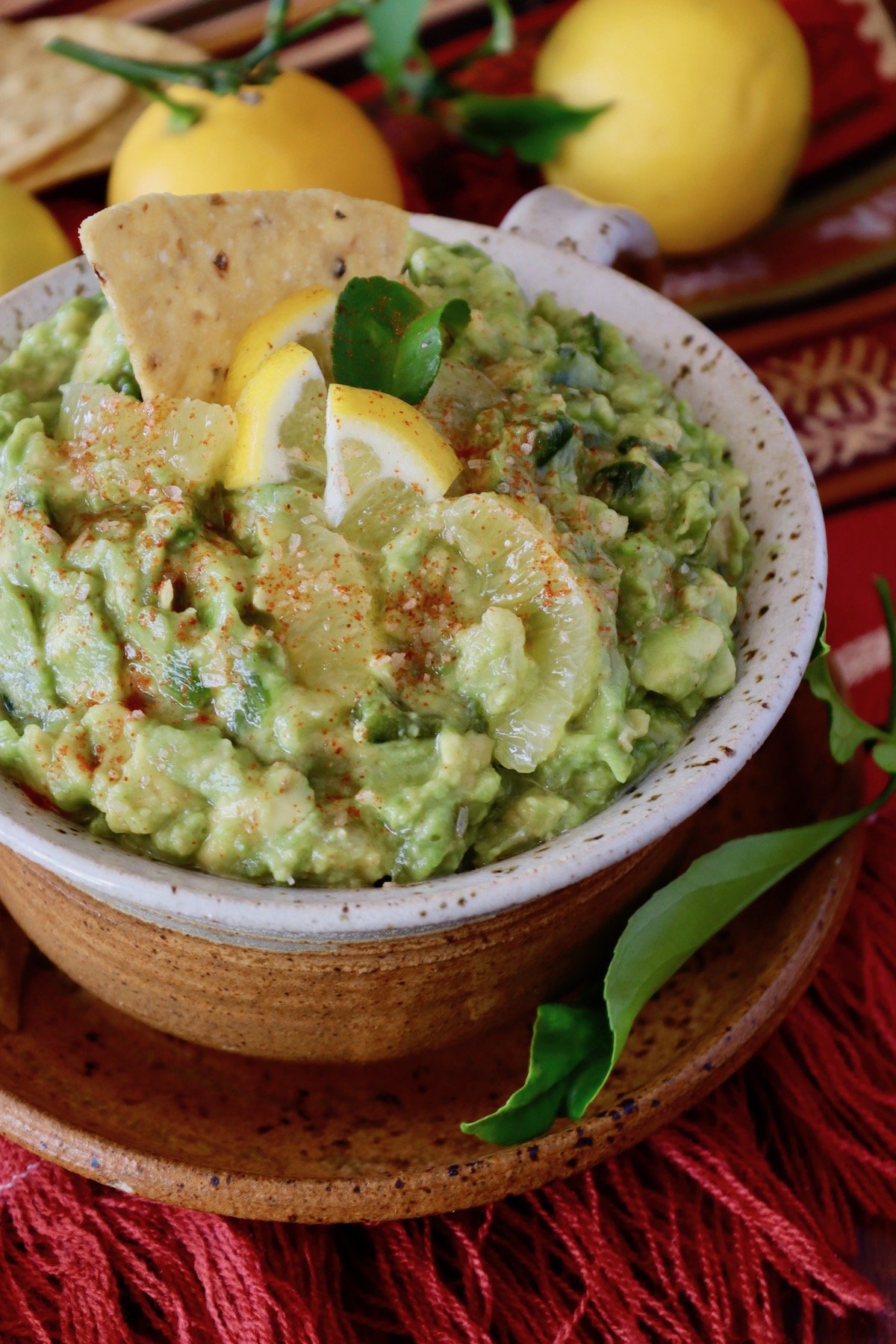 Close up of ceramic bowl full with poblano guacamole with lemons and a chip.