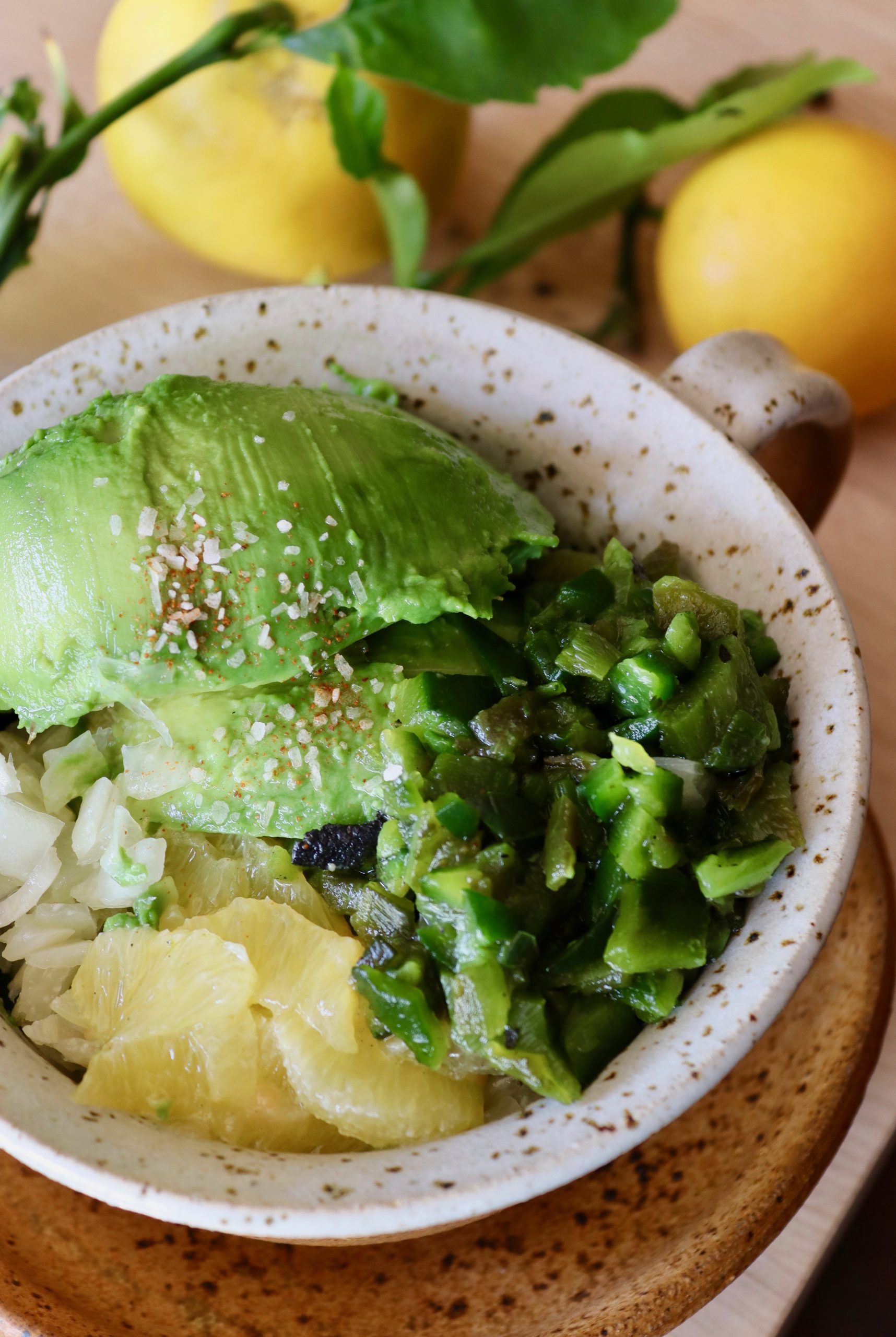 Ceramic speckled bowl filled with large pieces of avocado, lemon segments and chopped onion and green peppers.
