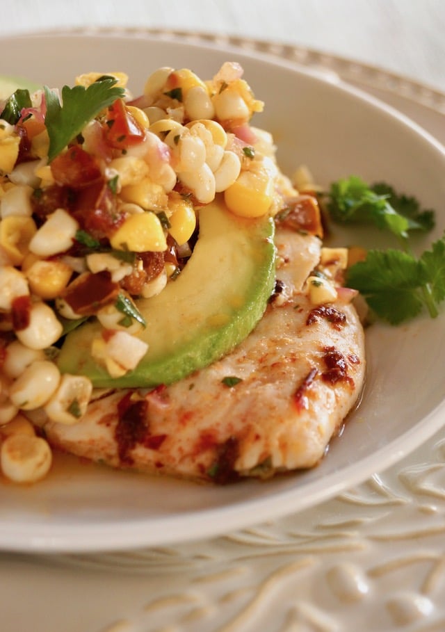 Close up of Sheet Pan Chipotle Chicken with Corn Salsa with an avocado slice on a white plate