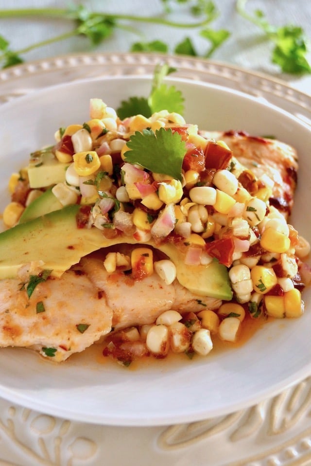 Sheet Pan Chipotle Chicken with Corn Salsa on a white plate with avocado and cilantro sprigs