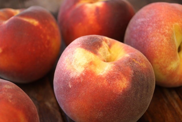 Several large red-yellow peaches on wooden surface.