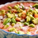 Easy Tomato Gazpacho recipe in a blue and white bowl with diced aocados, tomatoes and onion on top