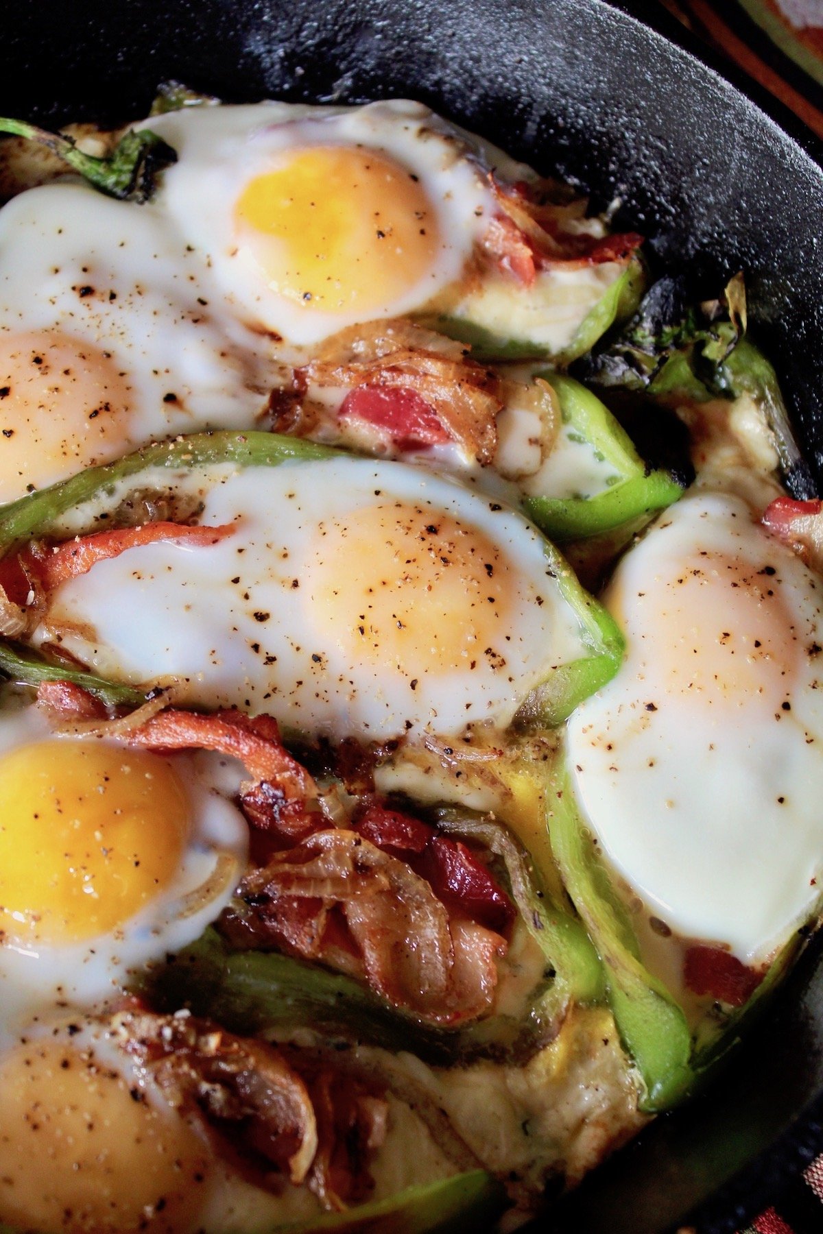 eggs on green chiles in cast iron skillet with bacon