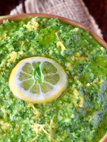 Green Lemon pesto with lemon slice and basil leaf on top, in a green bowl, fitted inside a yellow bowl.