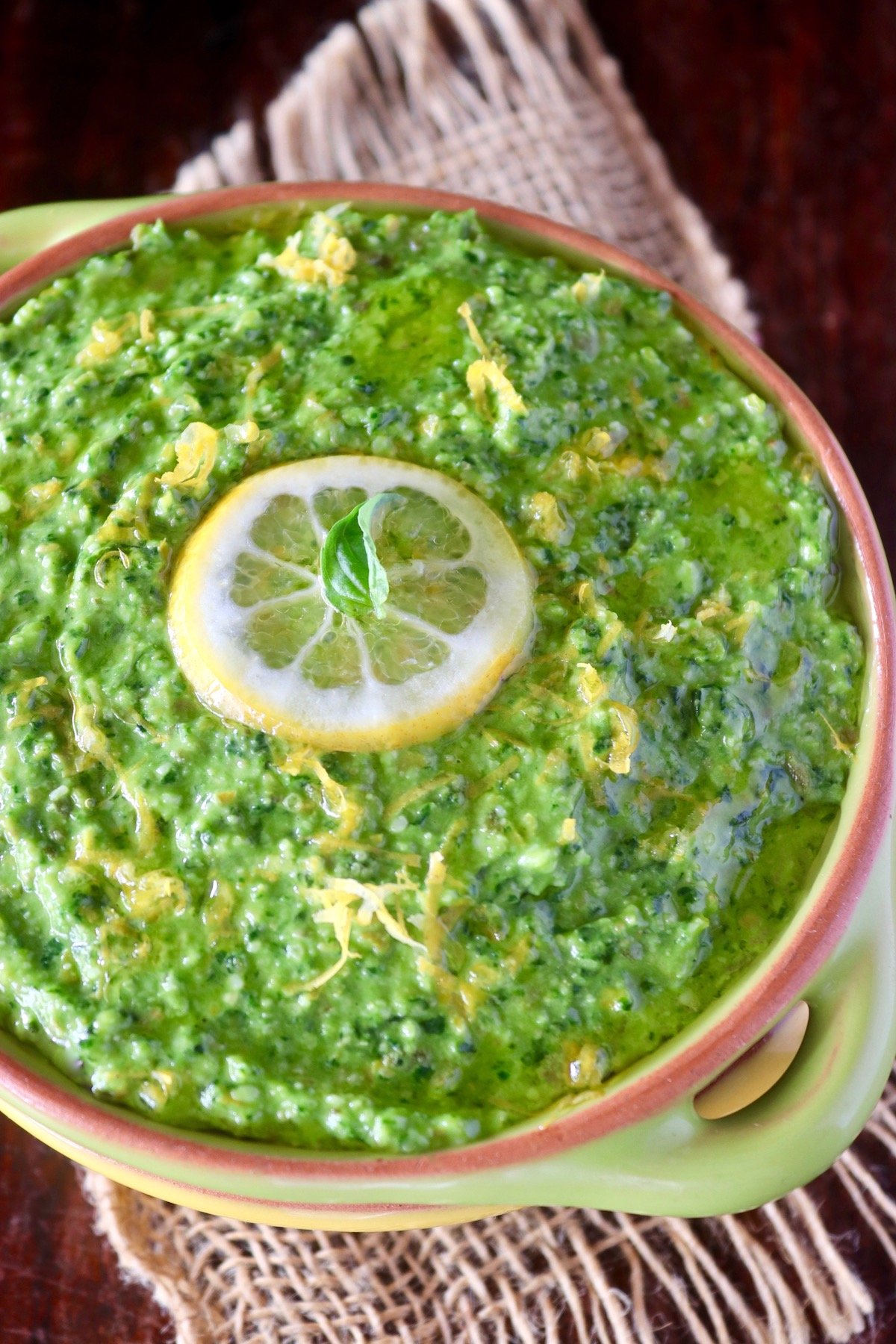 Green Lemon pesto with lemon slice and basil leaf on top, in a green bowl, fitted inside a yellow bowl.