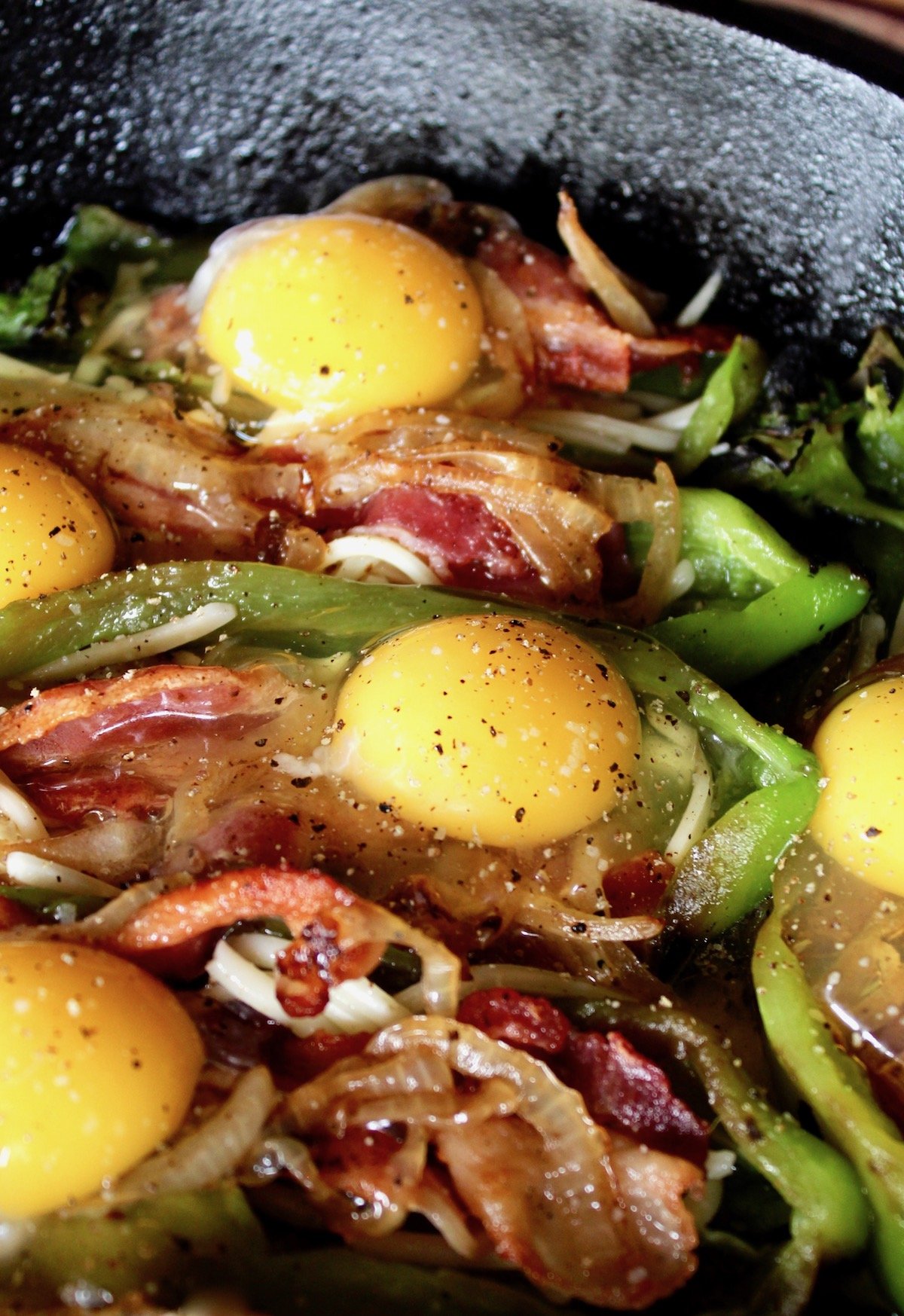 roasted hatch chiles in cast iron skillet with raw eggs and bacon