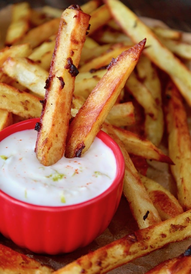 small red bowl with yogurt dip surrounded by curry fries and two in the dip 