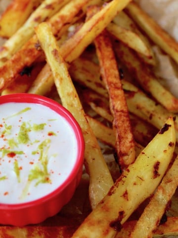 small red bowl with yogurt lime dip surround by French fries