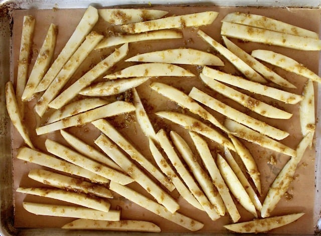 raw potato sticks on a sheet pan with curry paste