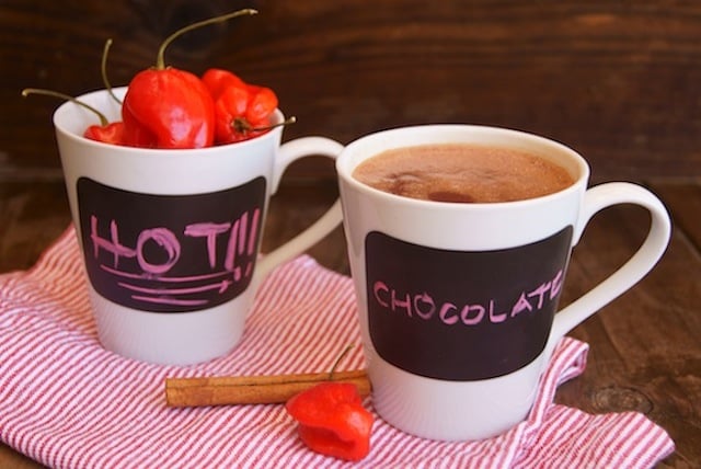 Spicy Mayan Hot Chocolate in a mug, with another mug full of red savina habanero peppers.