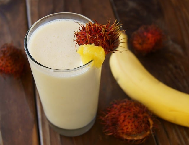 Tropical Smoothie in a tall glass with rambutan and pineapple on rim