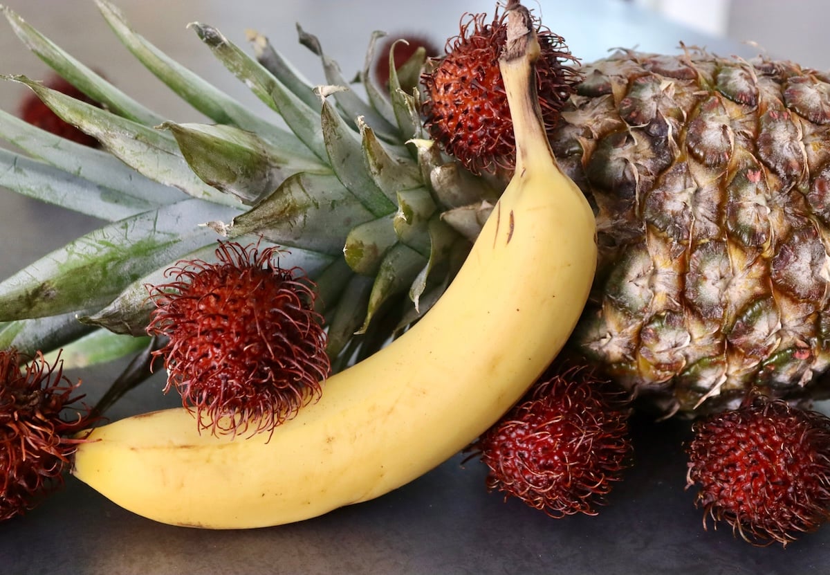 Banana, a few rambutans and a pineapple on a gray background.