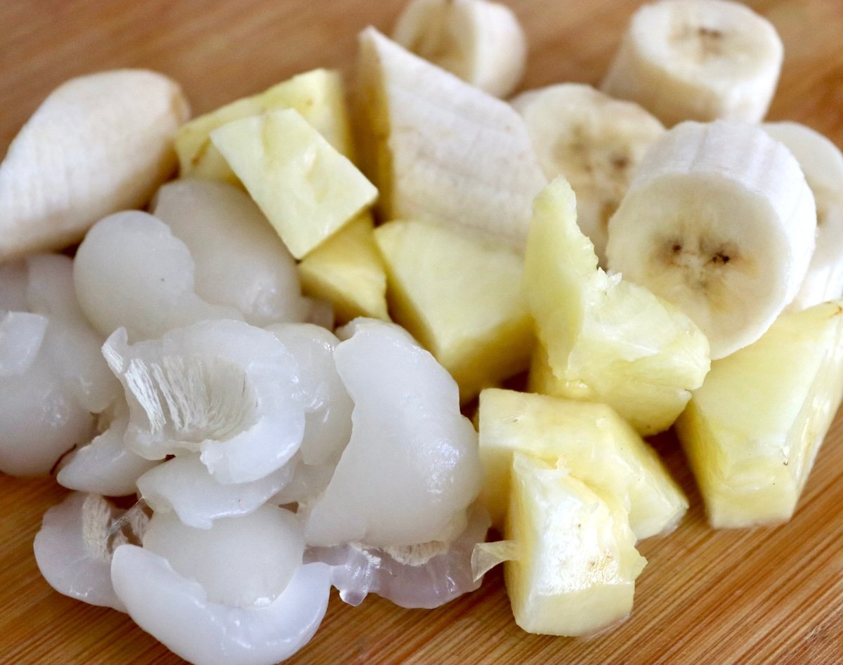 Cut banana, pineapple and rambutan on cutting board.