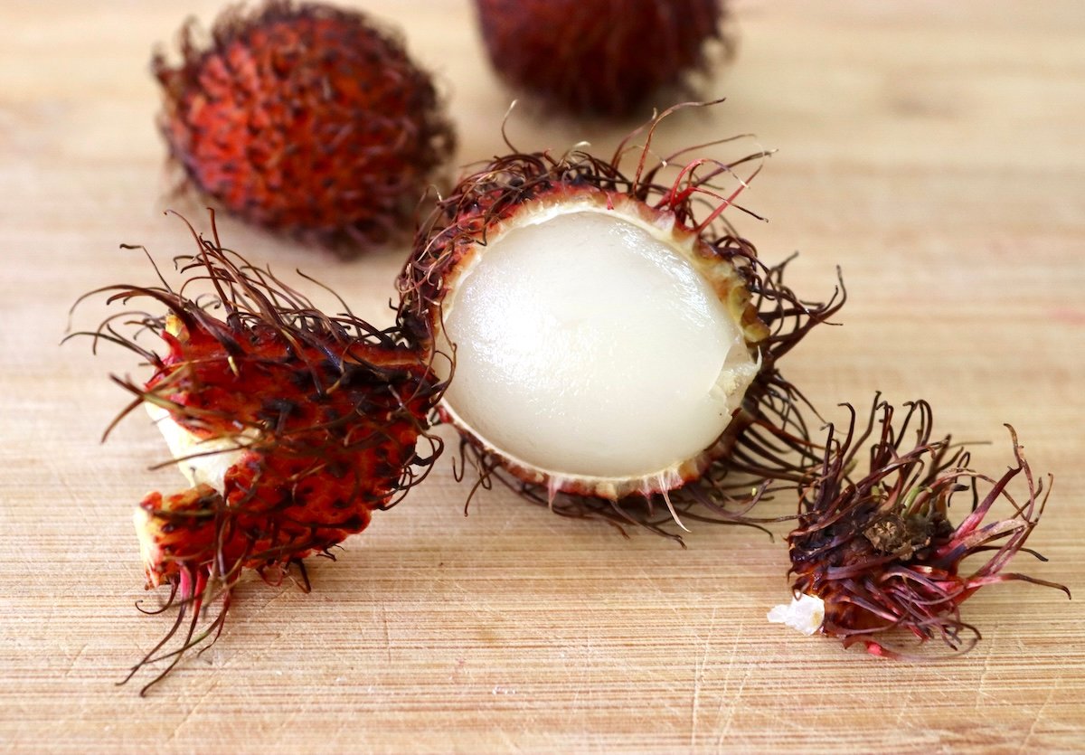 Rambutan with skin half peeled off on light wood cutting board.