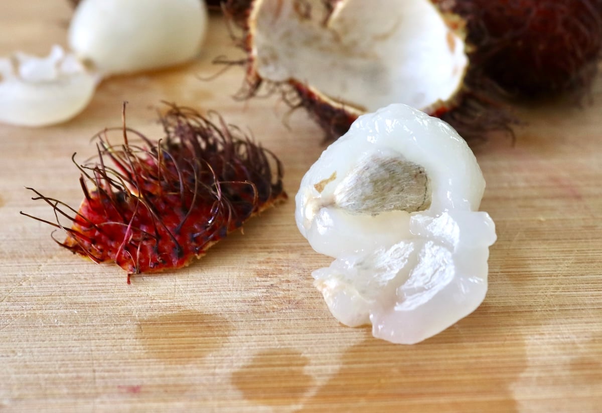 Peeled rambutan with white seed showing, on light wood cutting board.
